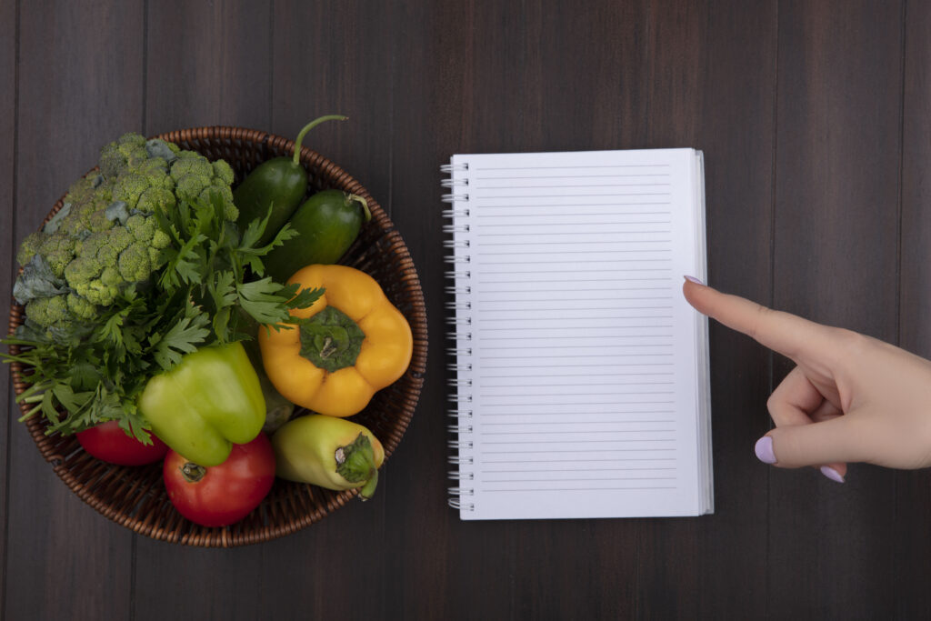 top view copy space woman points to copybook with bell peppers parsley and tomatoes in a basket on wooden background